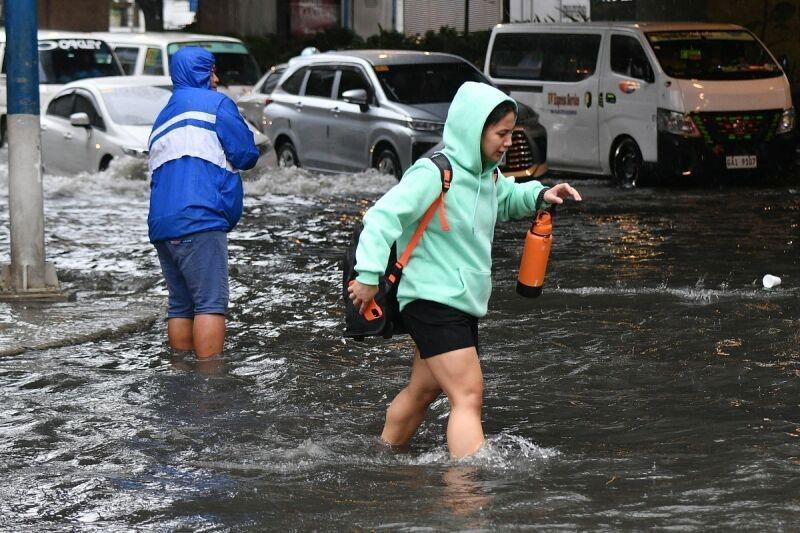 A pedestrian wades through a flooded street as a worker (L) unclogs a drainage in Manila on July 23, 2024, amid heavy rains brought about by Typhoon Gaemi (local name: Carina).